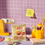 OHME! passion fruit snack pack on a desk with stationery items and a purple tiled wall.